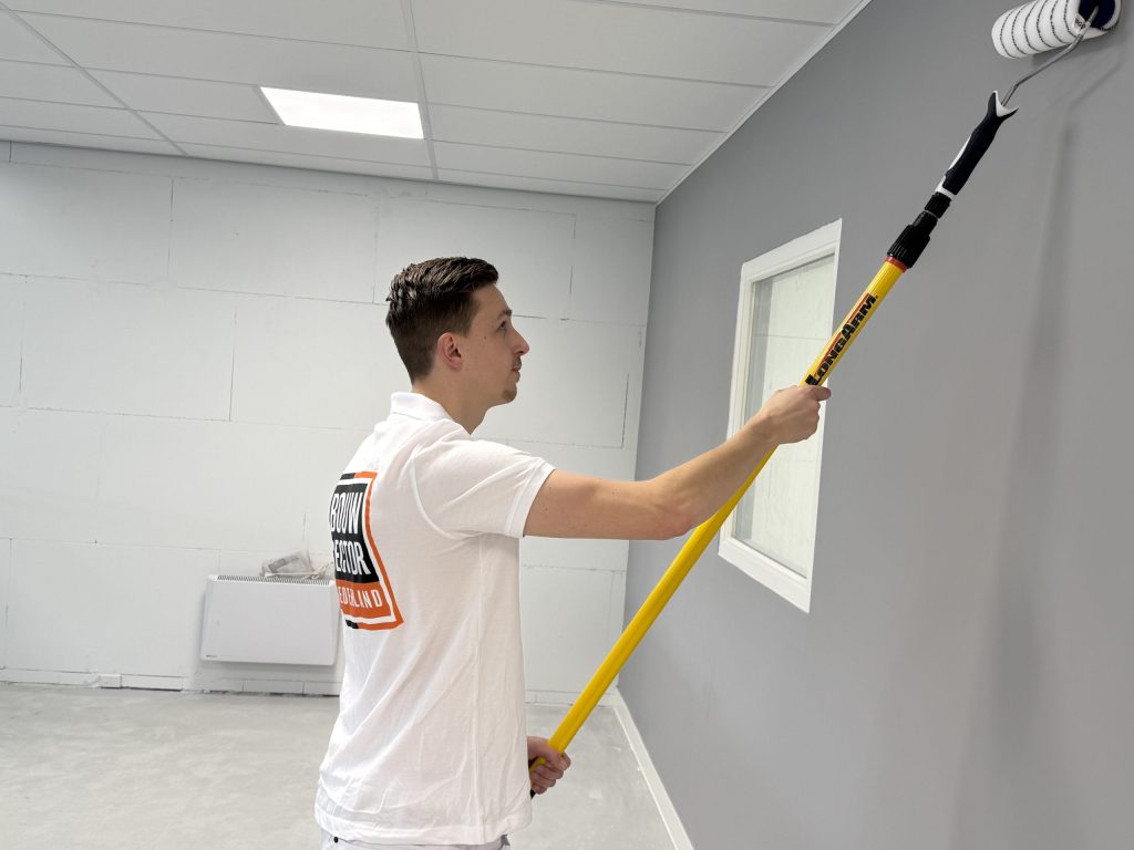 Schilder in wit poloshirt rolt een grijze wand naast een wit binnenraam