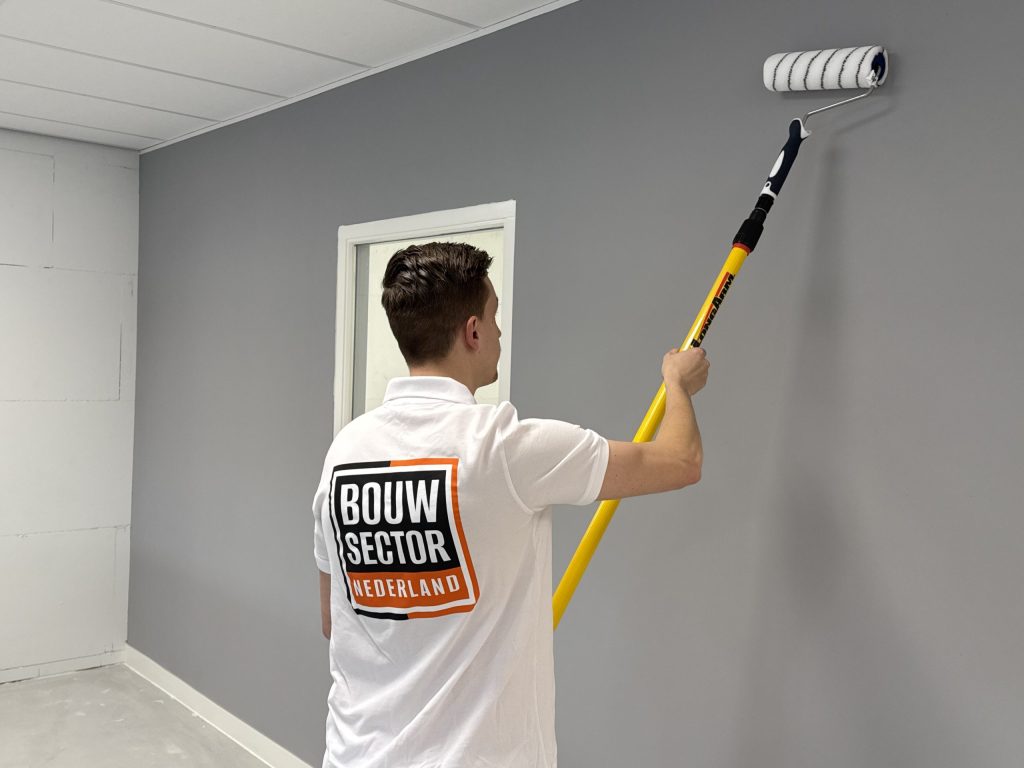 Schilder rolt een grijze muur onder een plafond van systeemplaten