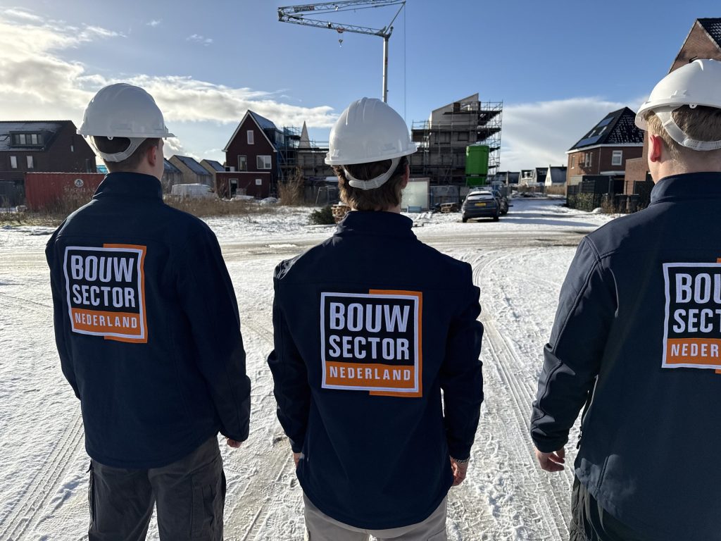 Drie vakmensen van Bouwsector Nederland in werkjas met helm bij nieuwe woningen